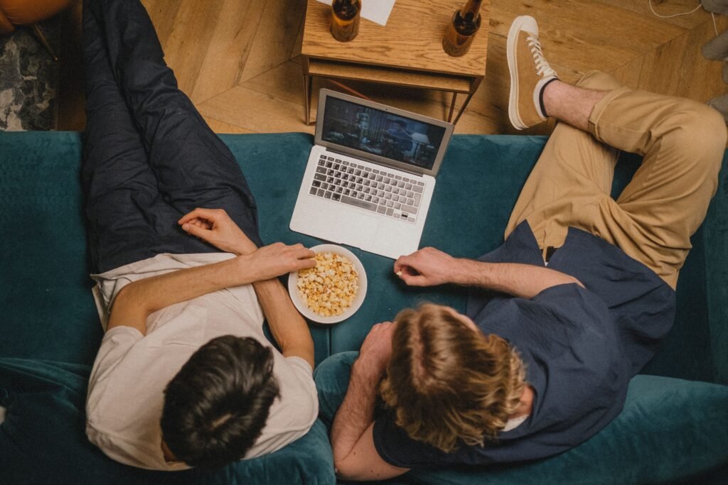 pexels-photo-9627169-9627169 Two friends enjoying a movie on a laptop with popcorn from a cozy couch perspective.